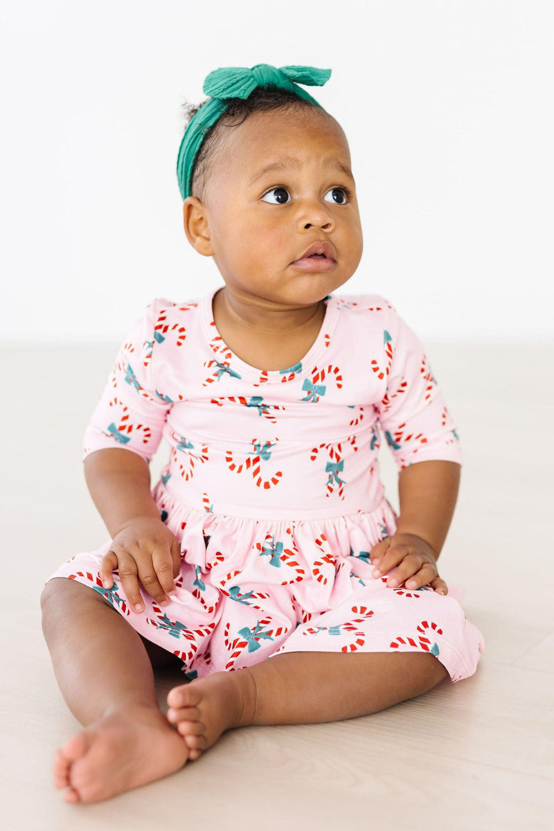 Baby wearing the Candy Cane Cutie 3/4 Sleeve Twirl Bodysuit with candy cane print, sitting and looking adorable in a cheerful setting.