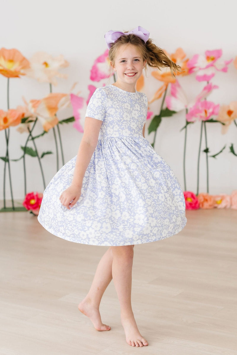 Little girl happily wearing the Blossom Bliss S/S Pocket Twirl Dress, twirling and showing off the dress's fun design.