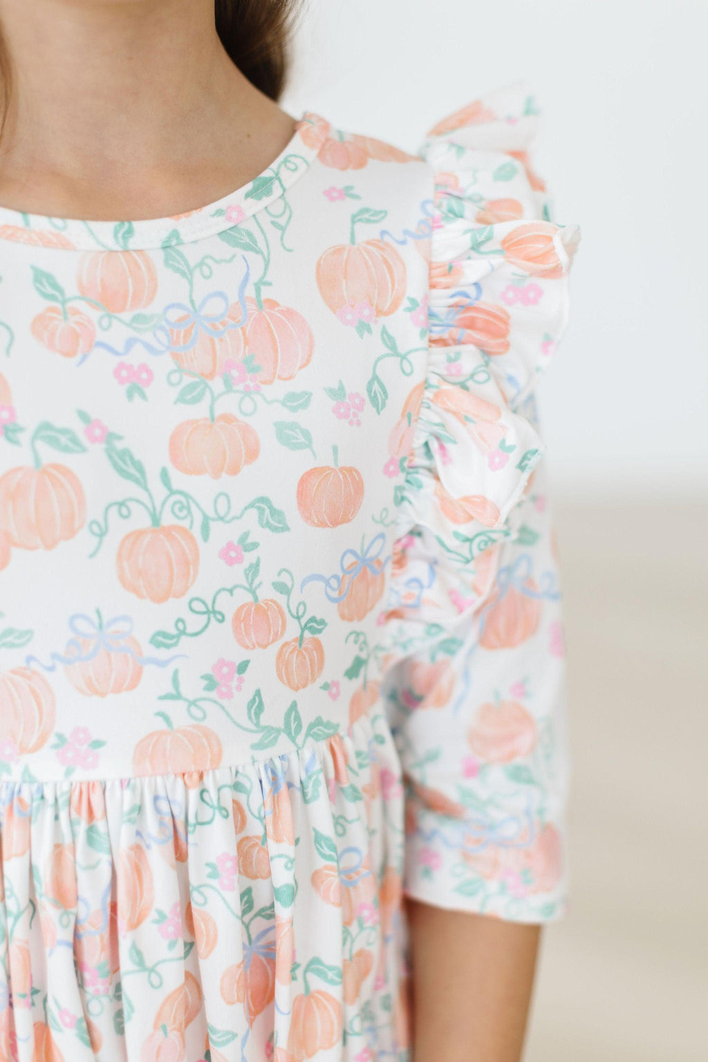 Pretty Pumpkins Ruffle Twirl Dress displayed on a playful child, showcasing twirl-friendly ruffles and fall-inspired pumpkin patterns, perfect for autumn adventures.