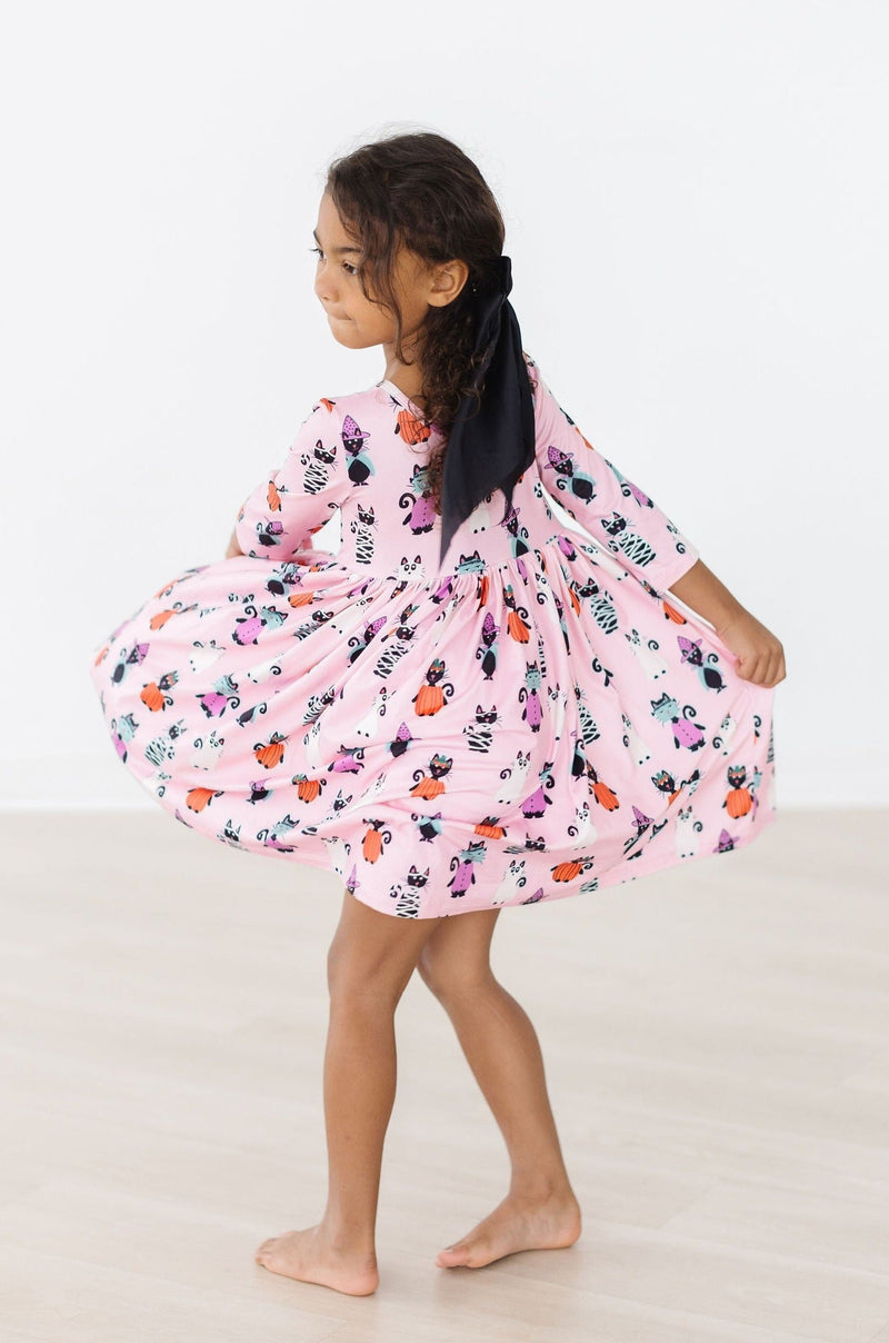 A child spinning gracefully in the Purr-fectly Spooky 3/4 Sleeve Pocket Twirl Dress, demonstrating the dress's twirl ability and fun design, perfect for Halloween play.