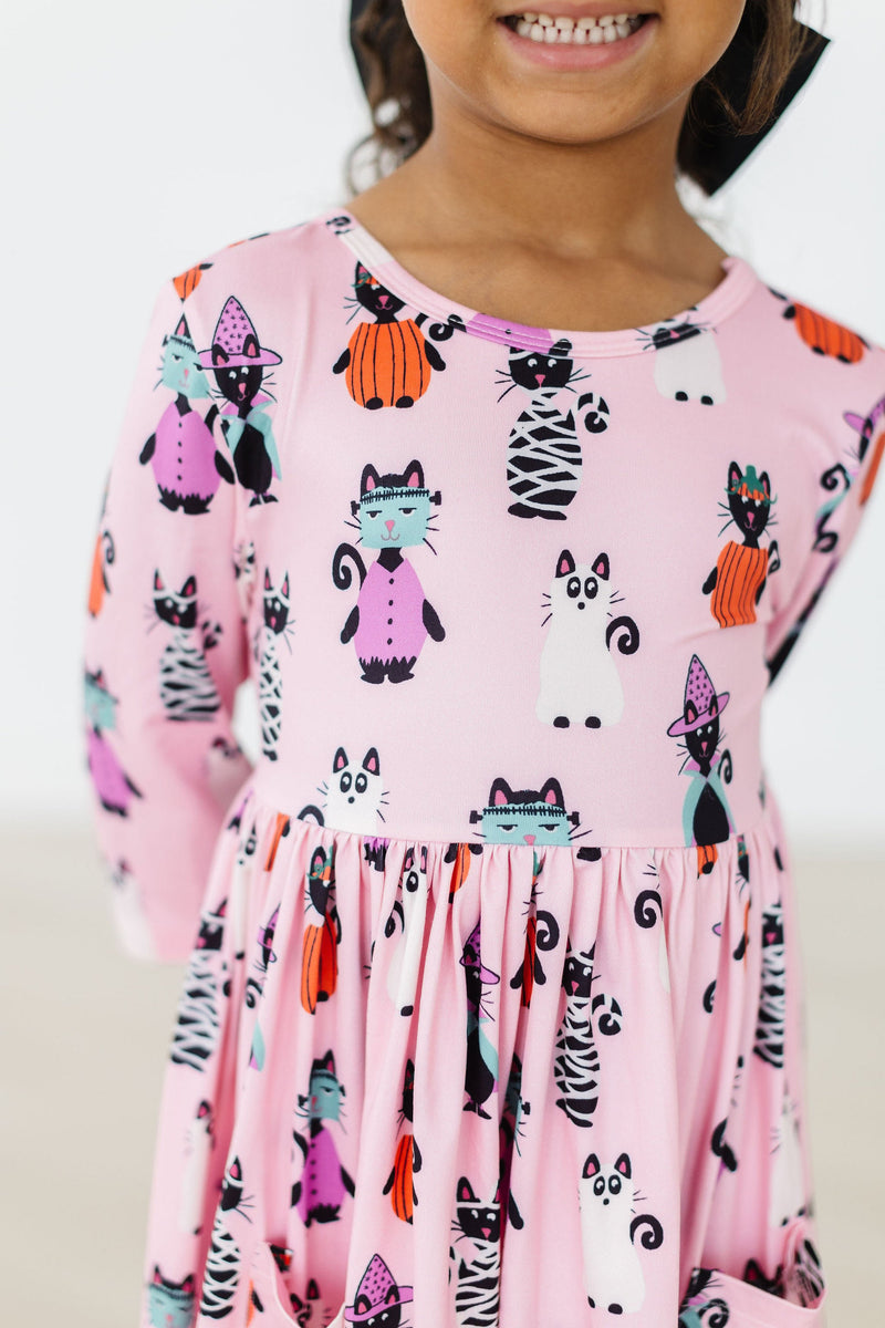 Close-up of a child wearing the Purr-fectly Spooky 3/4 Sleeve Pocket Twirl Dress, featuring cute cat and Halloween-themed prints, paired with a bright smile.