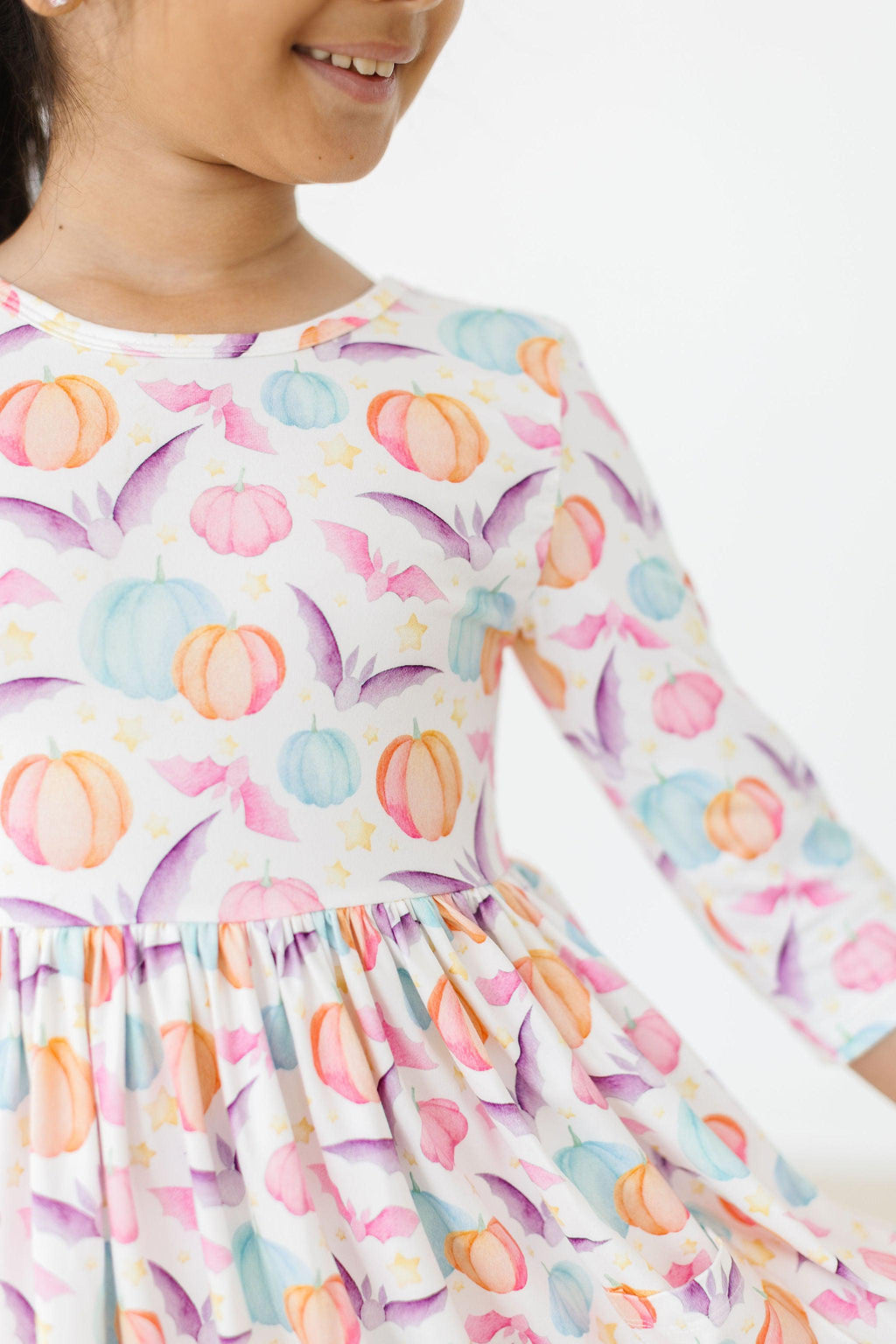 Girl smiling in the Spooky Sweetheart 3/4 Sleeve Pocket Twirl Dress featuring a colorful pumpkin and bat print, showcasing a playful design for Halloween fun.