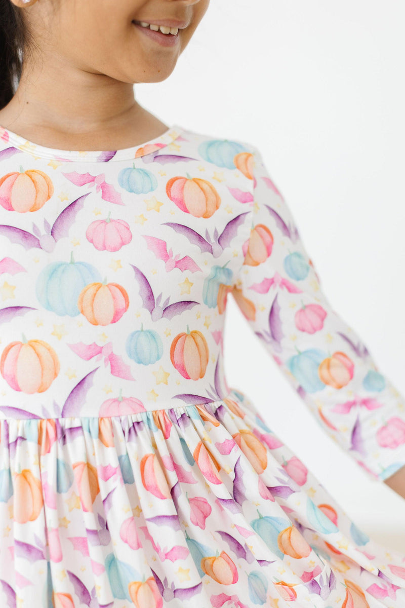 Girl smiling in the Spooky Sweetheart 3/4 Sleeve Pocket Twirl Dress featuring a colorful pumpkin and bat print, showcasing a playful design for Halloween fun.