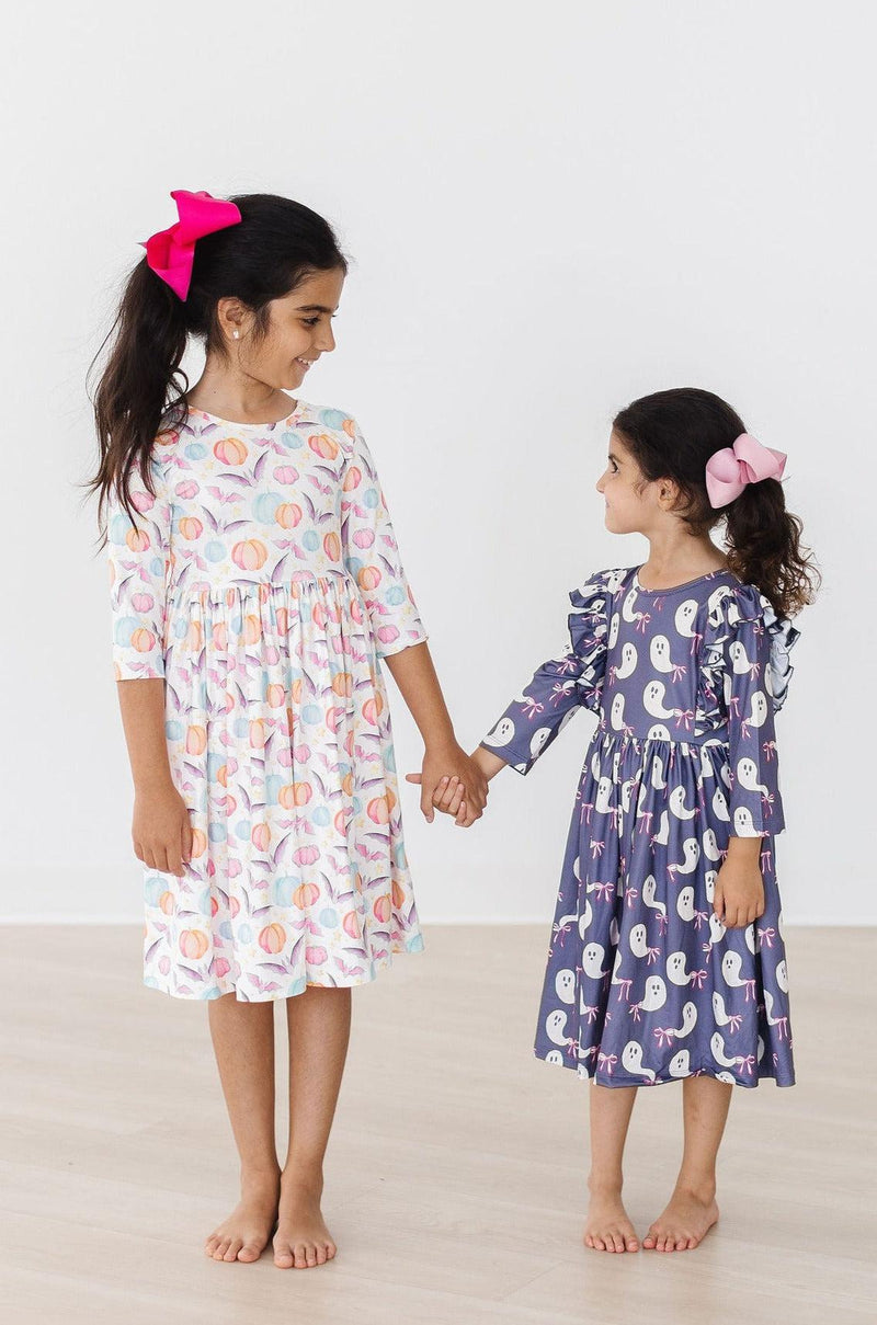 Two girls holding hands, one wearing the Spooky Sweetheart 3/4 Sleeve Pocket Twirl Dress and the other in a ghost-themed dress, perfect for playful Halloween celebrations.