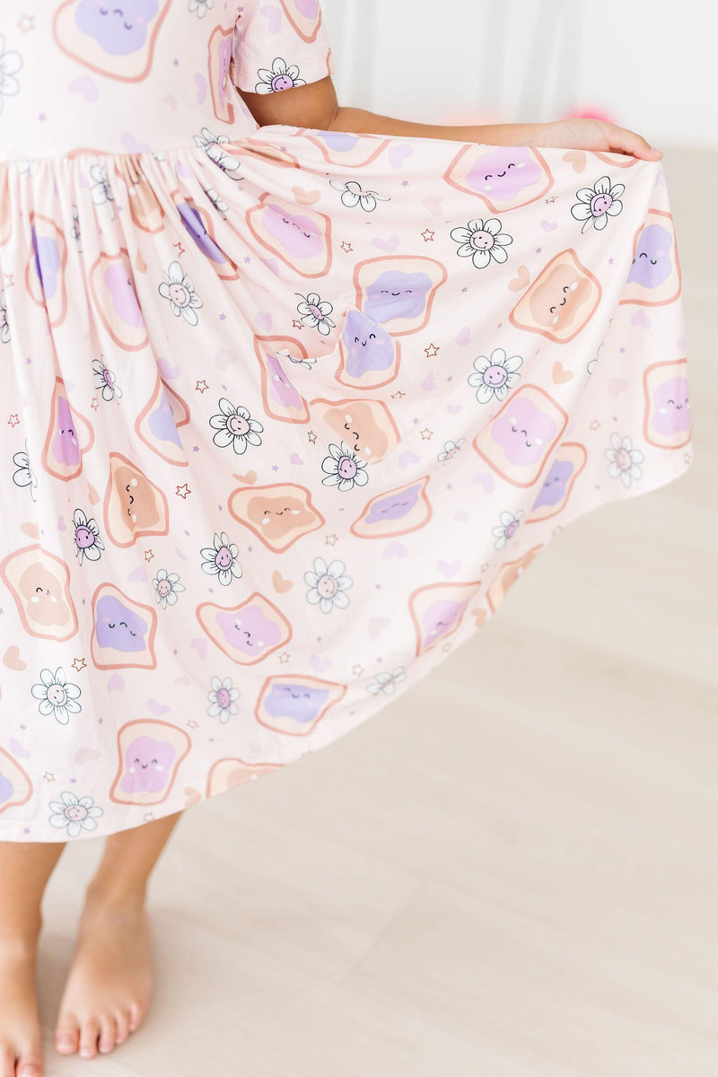 A detailed shot of the flared hem of the Peanut Butter Jelly Time S/S Pocket Twirl Dress by Mila & Rose, emphasizing the fun peanut butter and jelly print dancing around.