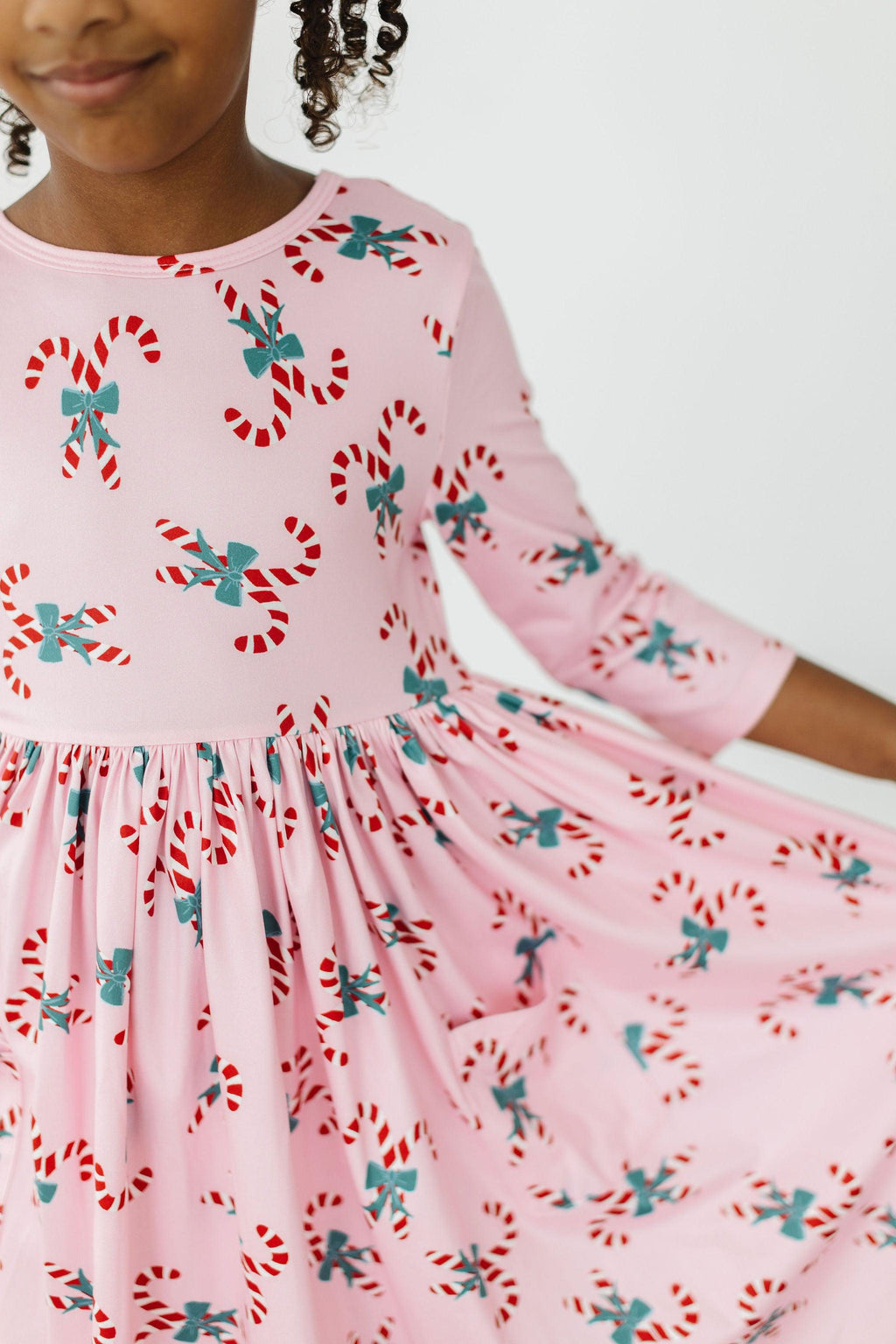 Candy Cane Cutie 3/4 Sleeve Pocket Twirl Dress featuring a pink fabric adorned with colorful candy cane prints, showcasing a playful twirl design perfect for festive occasions.