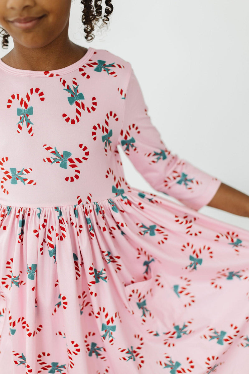 Candy Cane Cutie 3/4 Sleeve Pocket Twirl Dress featuring a pink fabric adorned with colorful candy cane prints, showcasing a playful twirl design perfect for festive occasions.