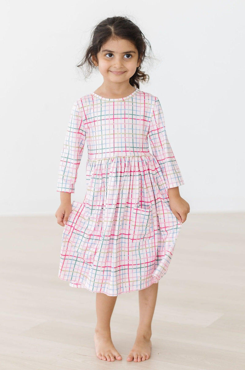 The same girl showcases the Pink Plaid 3/4 Sleeve Pocket Twirl Dress with its practical pockets, smiling confidently with a charming pose.