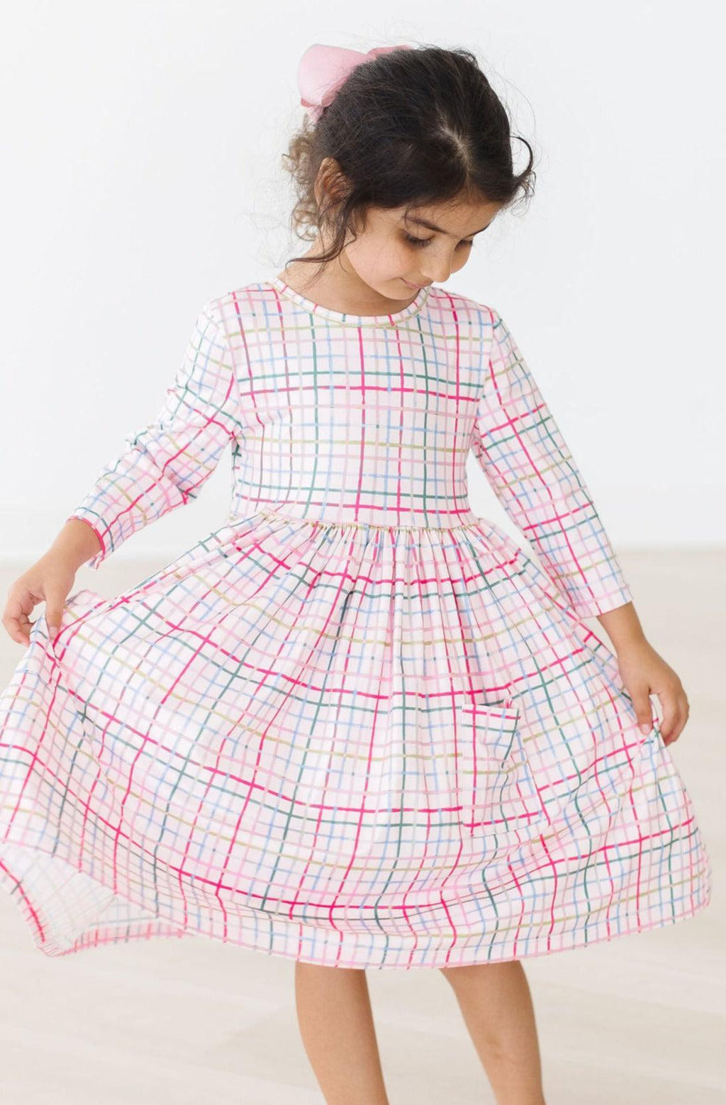 Little girl joyfully twirling in the Pink Plaid 3/4 Sleeve Pocket Twirl Dress, showcasing its playful design and comfortable fit.