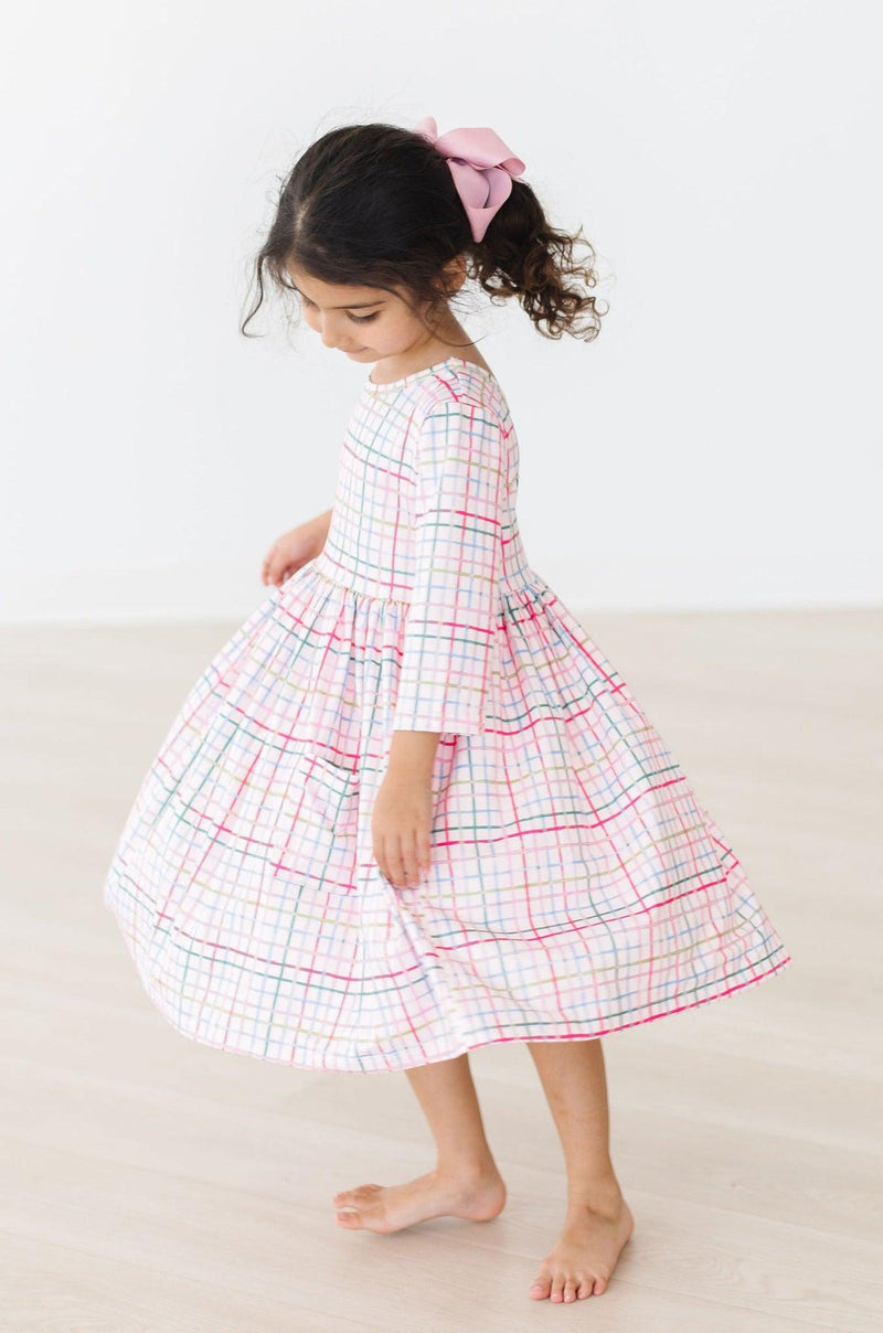 In a playful moment, a girl enjoys a twirl in her Pink Plaid 3/4 Sleeve Pocket Twirl Dress, capturing the fun and comfort ideal for any occasion.