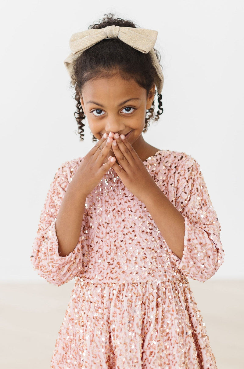 A young girl smiling with her hands over her mouth, wearing the elegant Rose Gold Velvet Sequin Dress, capturing a joyful moment.