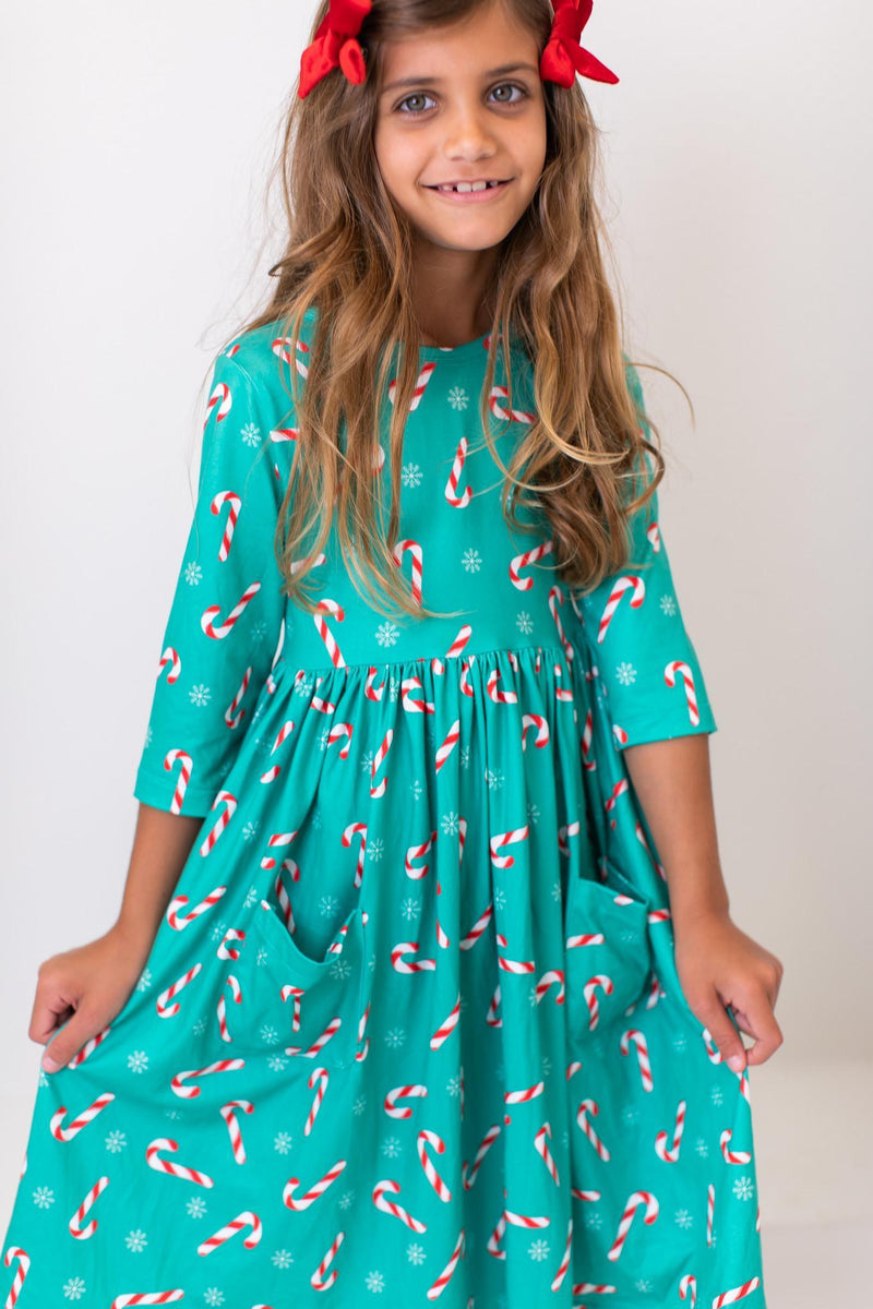 Close-up of a girl in a Christmas Candy 3/4 Sleeve Pocket Twirl Dress by Mila & Rose, showcasing its playful candy cane print and convenient front pockets.
