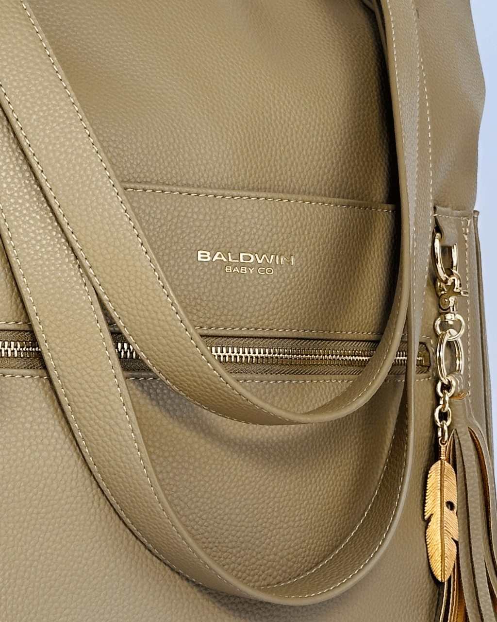 Front zippered pocket on taupe bag displaying gold foil stamped Baldwin Baby Co logo and tassel
