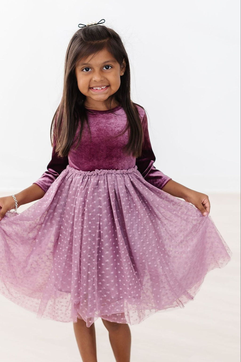 A cheerful girl wearing an Amethyst Velvet Tutu Dress with 3/4 sleeves and a tulle skirt, twirling with joy. Perfect for special occasions.