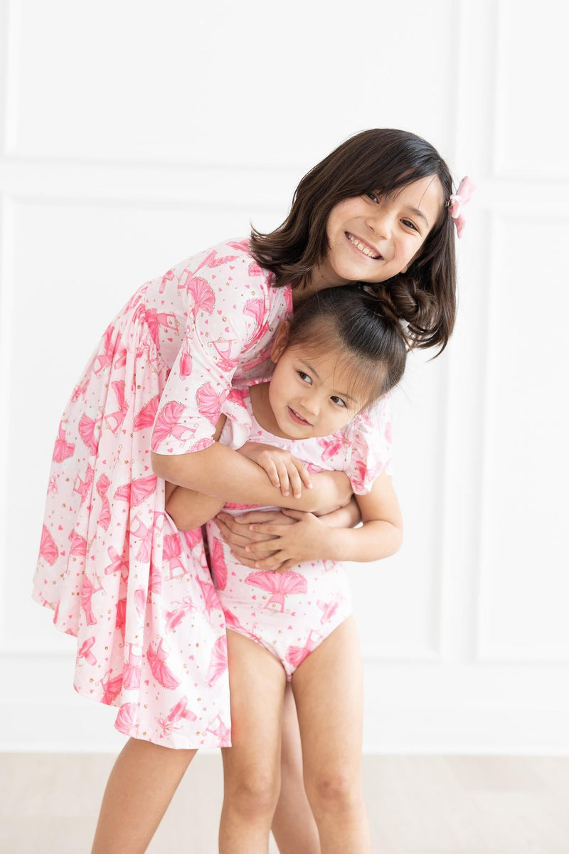 A happy moment between sisters as one wears the Pirouette 3/4 Sleeve Pocket Twirl Dress and the other is in a matching outfit, showcasing their playful bond.