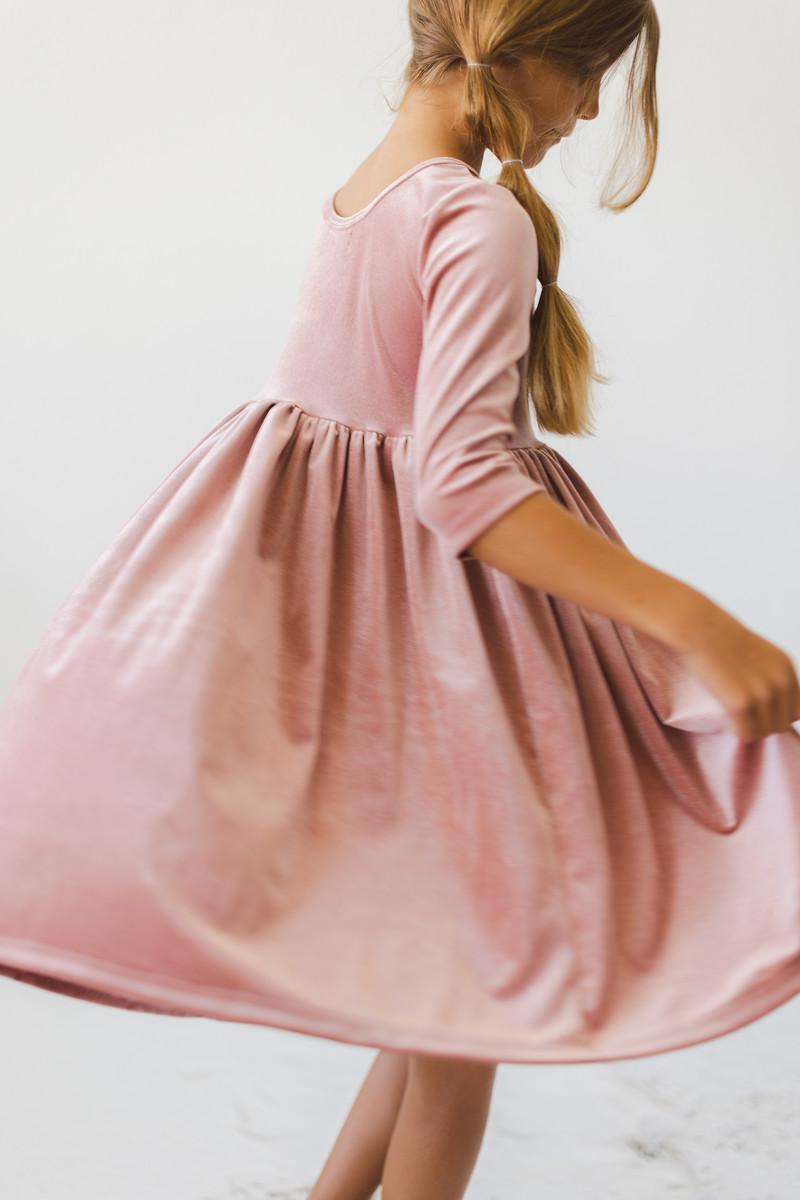 A young girl twirling in a Vintage Pink Velvet Twirl Dress, showcasing the soft fabric and full skirt, perfect for playful moments and special occasions.