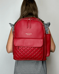 Crimson vegan leather diaper bag featuring a quilted front pocket with silver studs and a side sleeve, worn as a stylish backpack.