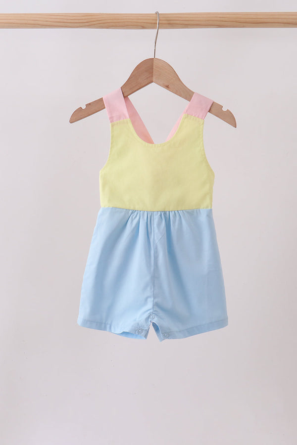 Pastel-colored baby romper with pink straps hanging on a wooden hanger against a light background