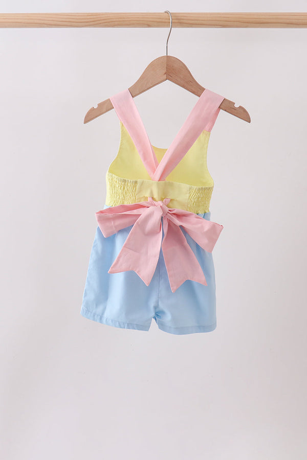 Pastel-colored children's outfit with a pink bow on a hanger against a white background