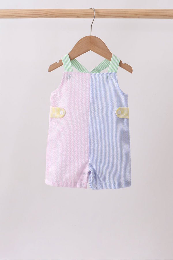 Two children's dresses, one pink and one blue with white stripes, hanging on a wooden hanger against a light gray background.