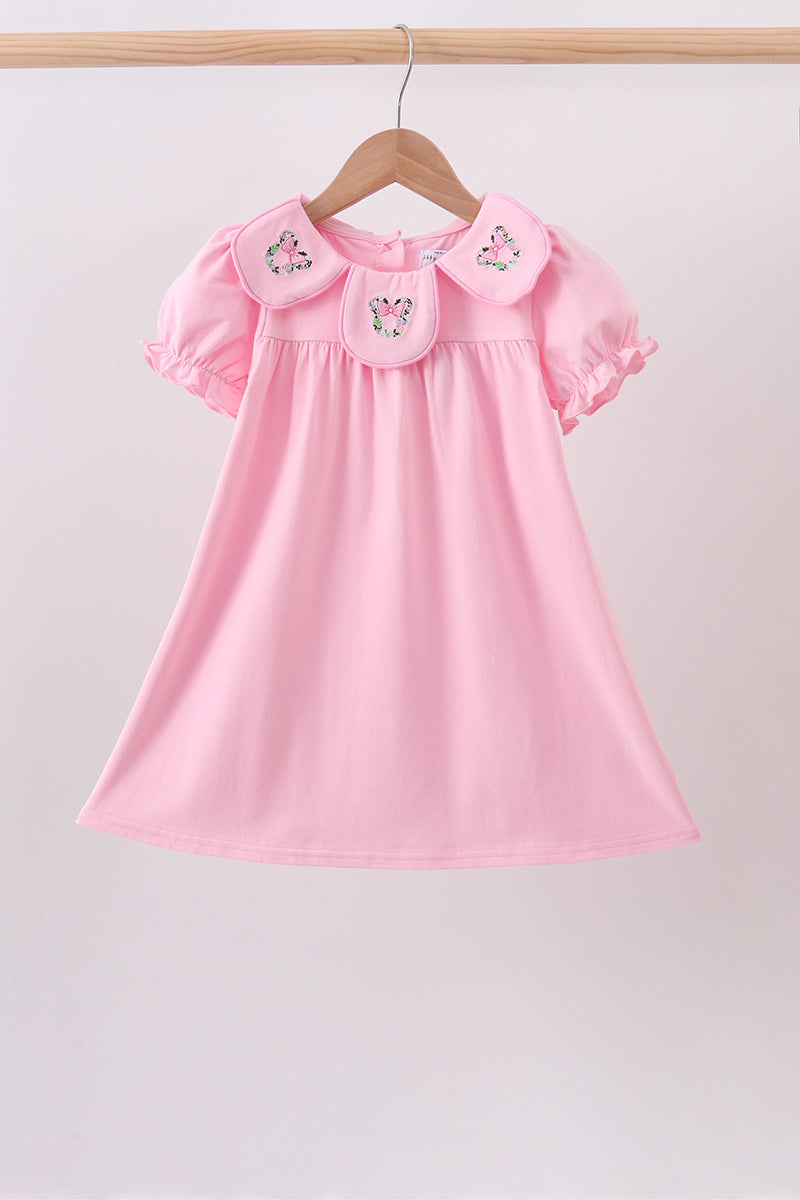 Pink dress with floral embroidery on Peter Pan collar and puff sleeves, hanging on a wooden hanger.