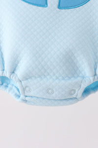 Light blue quilted baby bubble onesie featuring three snap closures at the crotch and a decorative blue appliqué trim at the neckline.