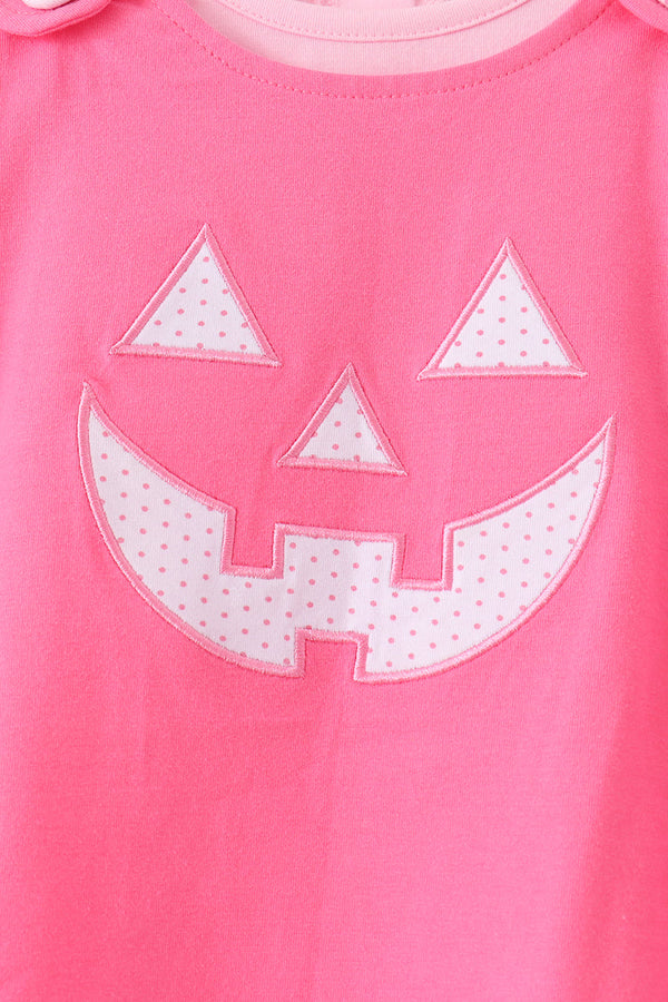Pink Jack-O-Lantern applique on pink Halloween dress featuring white polka dot pumpkin face detailing for festive wear.