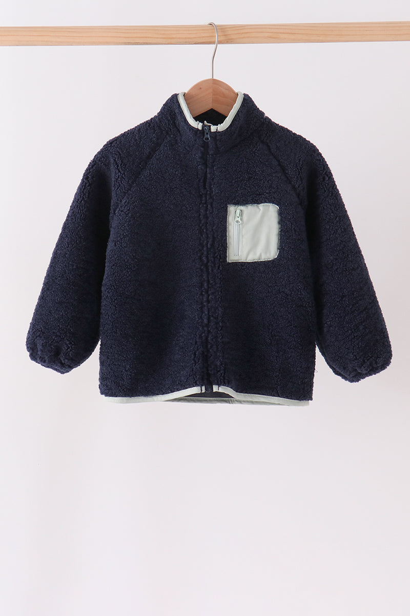 Navy fleece zipper jacket with light gray trim and zippered chest pocket hanging on a wooden hanger. Cozy warmth without bulk.