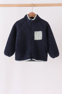 Navy fleece zipper jacket with light gray trim and zippered chest pocket hanging on a wooden hanger. Cozy warmth without bulk.