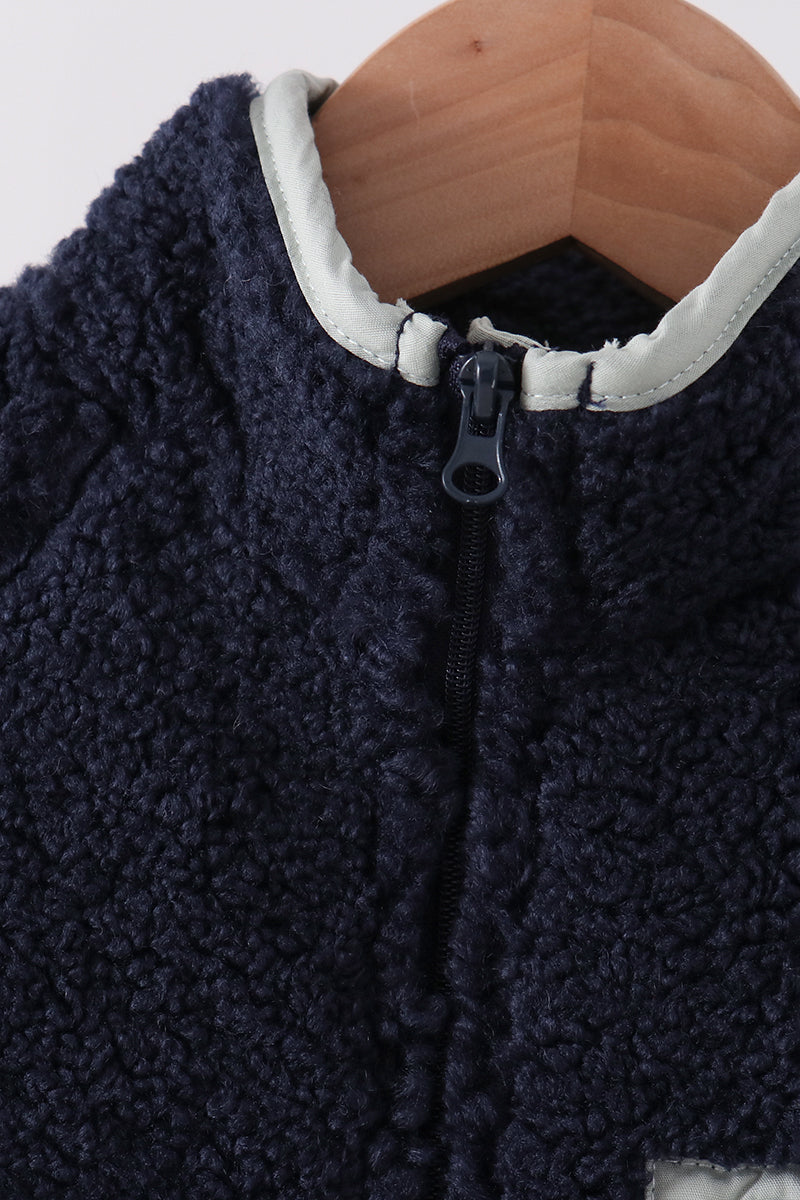 Navy fleece zipper jacket collar close-up showing soft texture, full front zip, and light trim on wooden hanger.