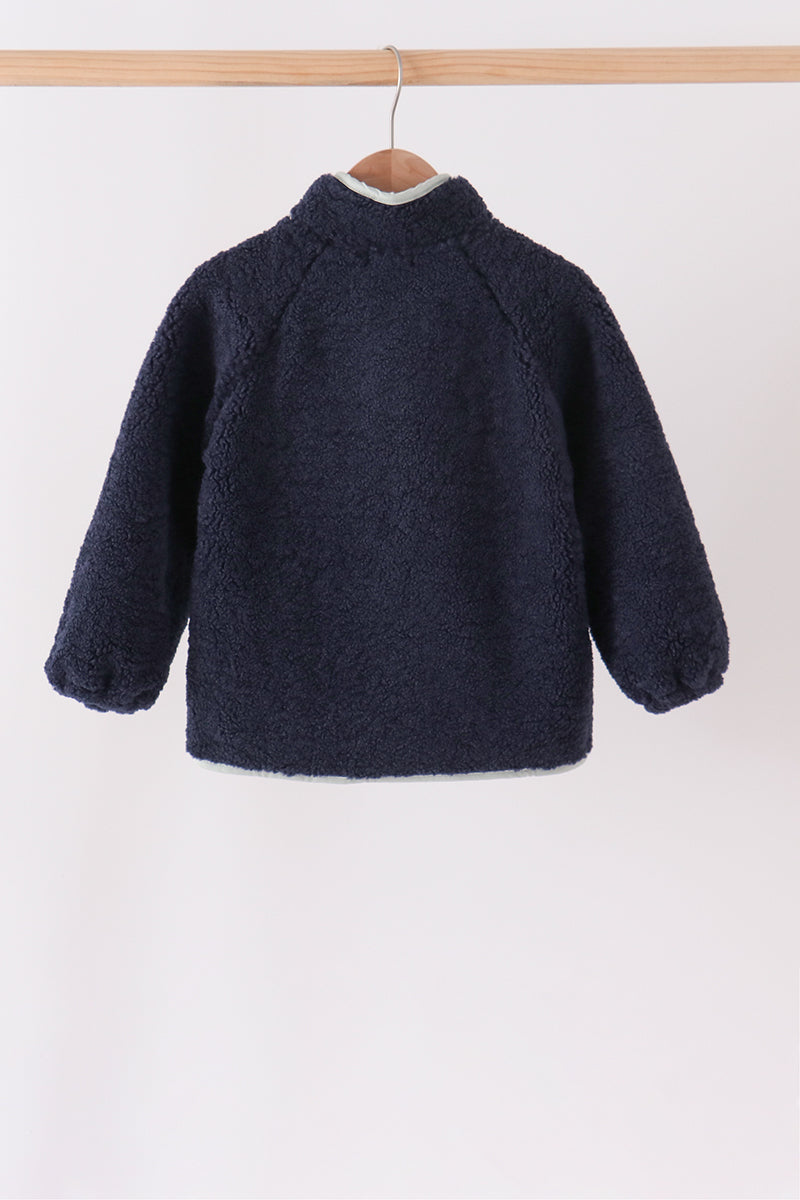 Back view of a navy fleece zippered jacket hanging on a wooden hanger, featuring a soft textured collar and cozy warmth for layering.