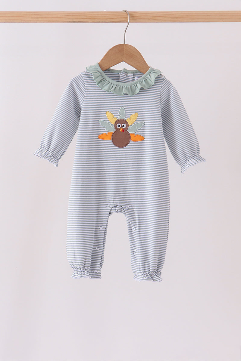 A baby long-sleeve romper with thin gray and white stripes, featuring a ruffled mint green collar and a central turkey applique on the chest, hanging on a wooden hanger against a light beige background.