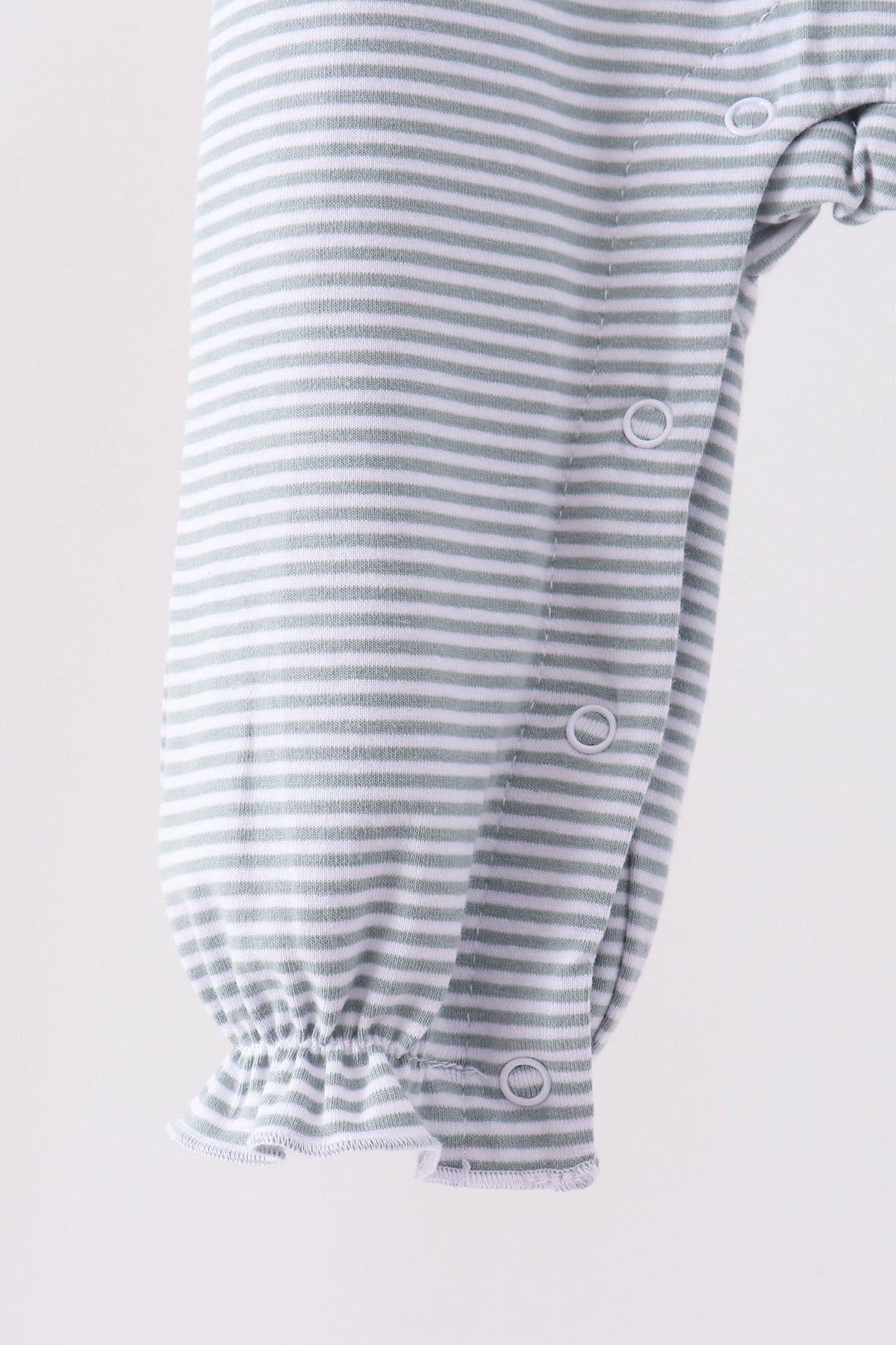 Close-up of a baby garment with fine gray and white horizontal stripes, featuring a gathered elastic cuff and snap closures along the side.