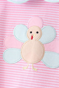A close-up of a pink and white striped fabric featuring an applique turkey design with pastel pink and light blue wings and a beige body.