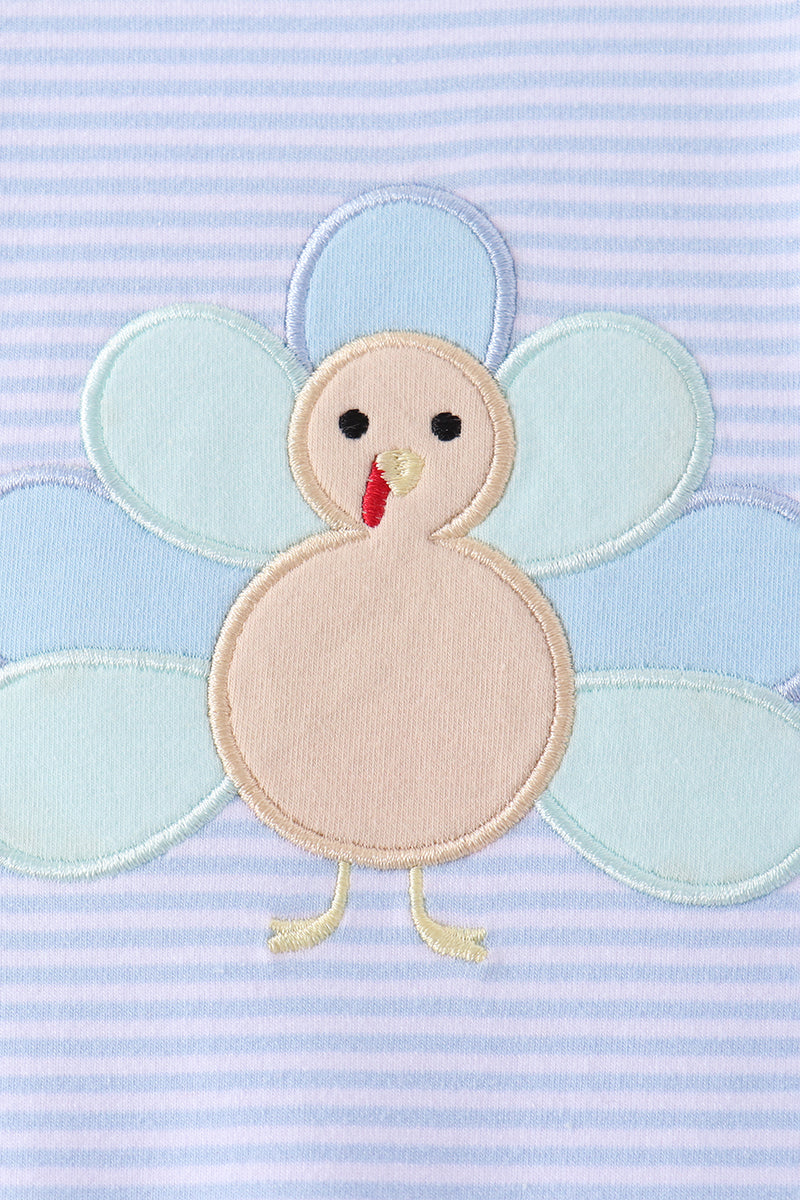 Close-up of whimsical turkey appliqué with blue and teal feathers on striped blue romper fabric.