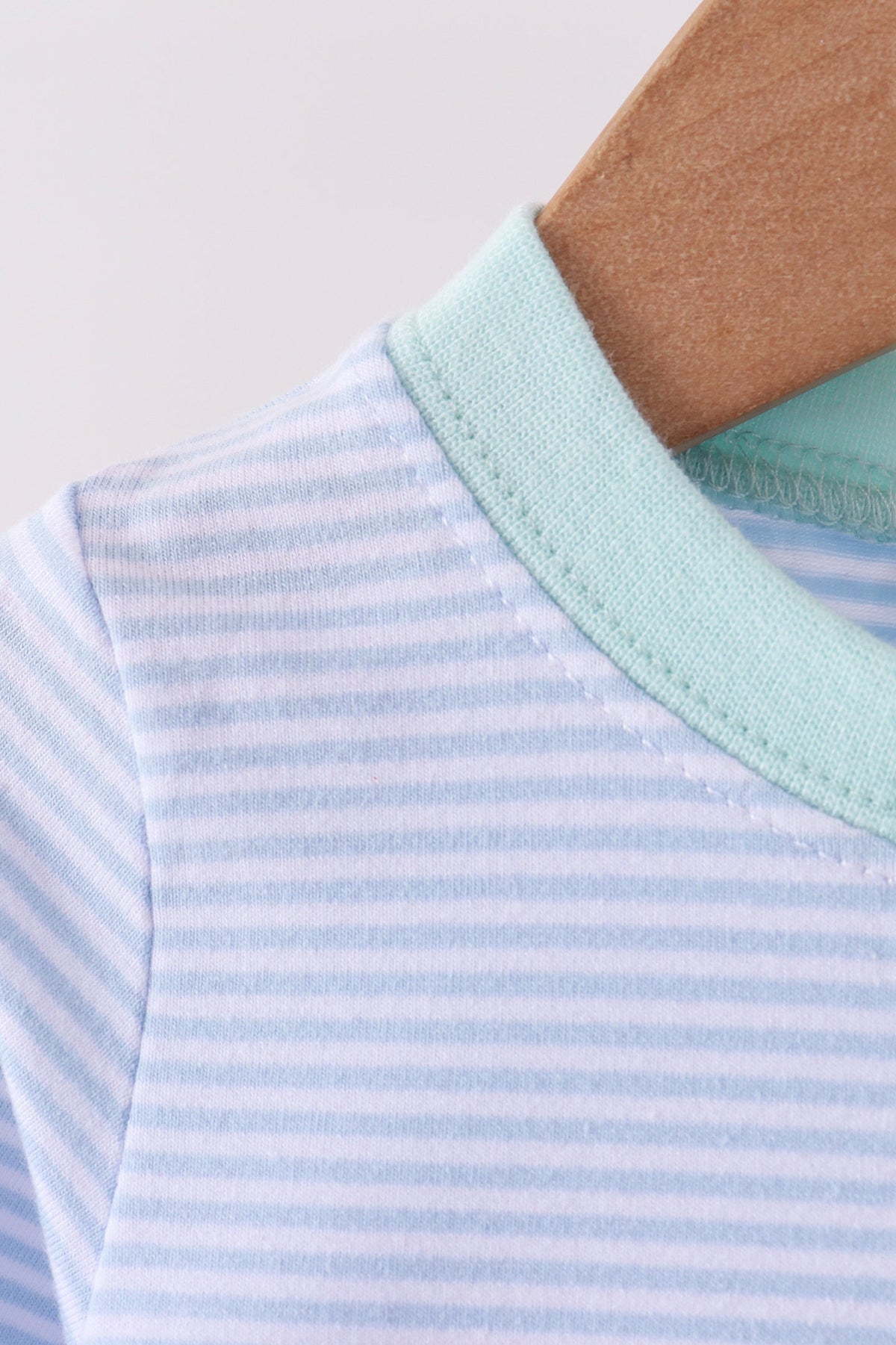 Blue and white stripe romper with mint green collar hanging on wooden hanger, soft striped fabric detail.