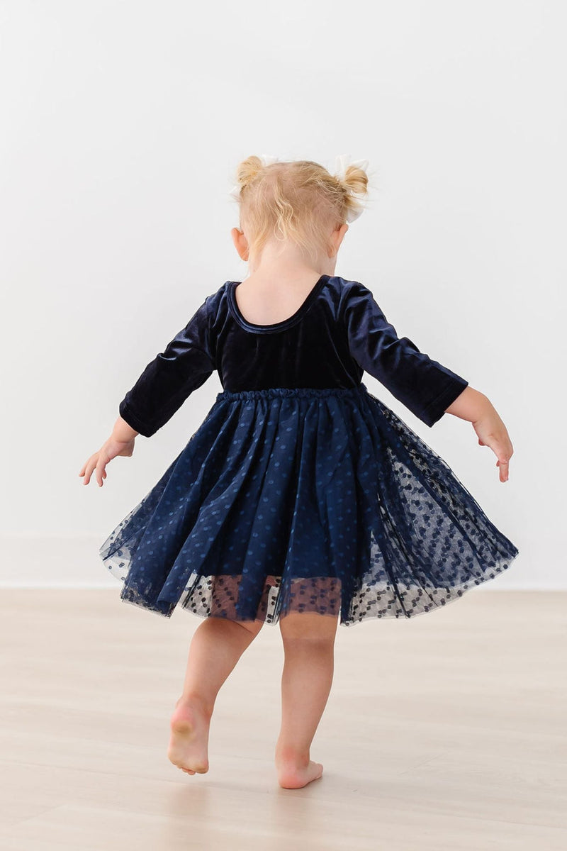 A cute toddler in the Light Navy Velvet Tutu Dress, spinning around playfully, highlighting the adorable scoop back and full tulle skirt against a minimalist background.