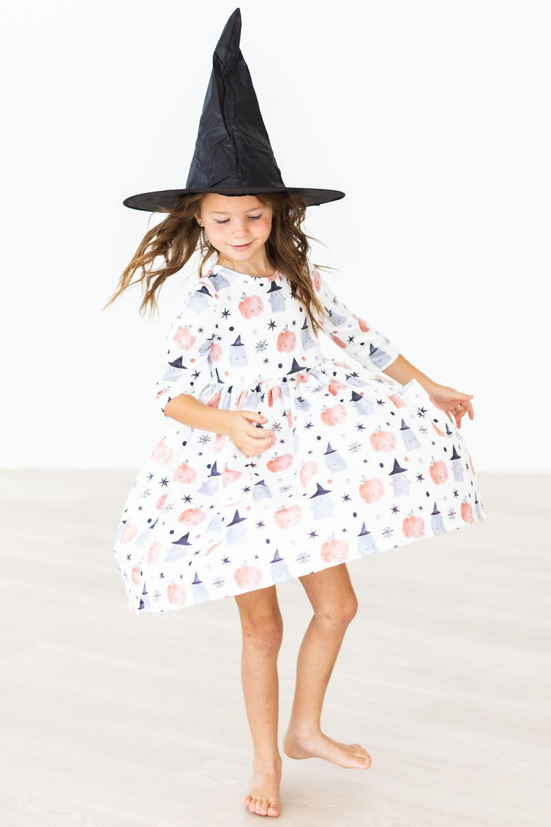 A joyful child spinning in the Peek-a-Boo 3/4 Sleeve Pocket Twirl Dress and a black witch hat, bringing magic and charm to playful moments.