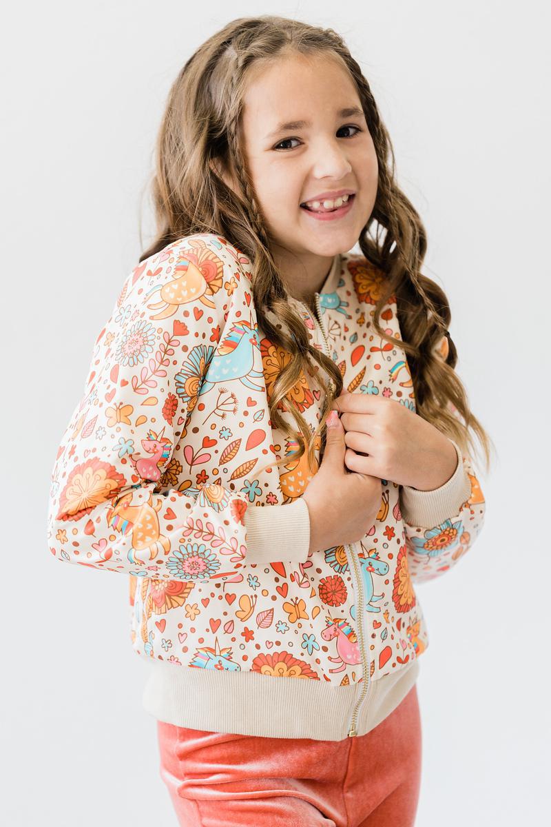 Cheerful girl wearing the 'Retro Unicorns' satin jacket for girls, showcasing its stylish design while smiling at the camera.