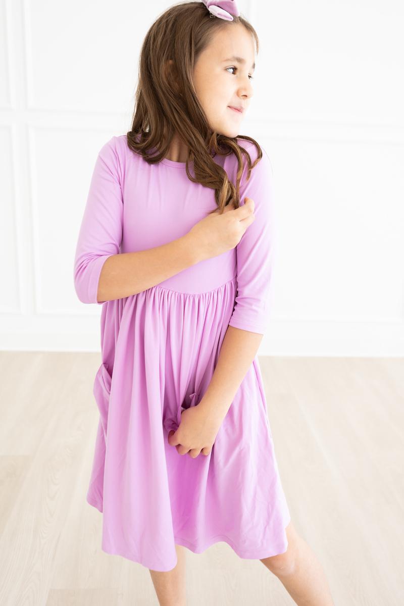 A girl joyfully twirling in the Bright Lilac 3/4 Sleeve Pocket Twirl Dress, embodying fun and freedom in a stylish outfit.