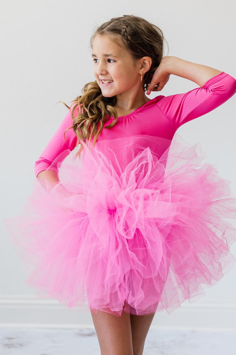 A young girl smiling while wearing a Hot Pink 3/4 Sleeve Fluffy Tutu Leotard for Girls. The leotard features a fluffy tulle skirt that enhances her graceful movements, making it an ideal tutu leotard for girls.