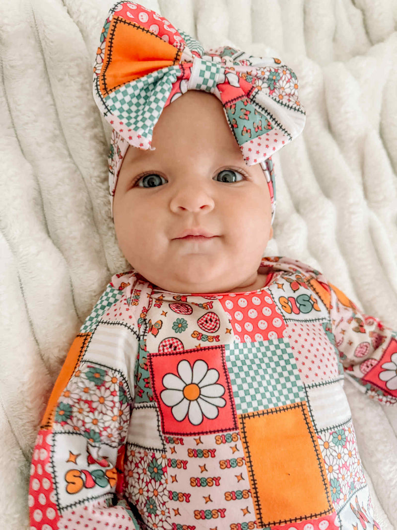 Close up of a cute baby in the Anti-Kick 'Sissy' Swaddle Gown & Headband 2 PC Set, featuring vibrant patterns and a matching headband. Ideal baby swaddle gown for precious photo moments.