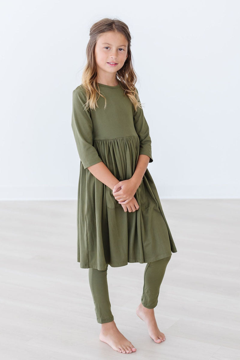 Olive 3/4 Sleeve Pocket Twirl Dress displayed on a girl posing with a subtle smile, highlighting its comfortable fit and stylish pockets.