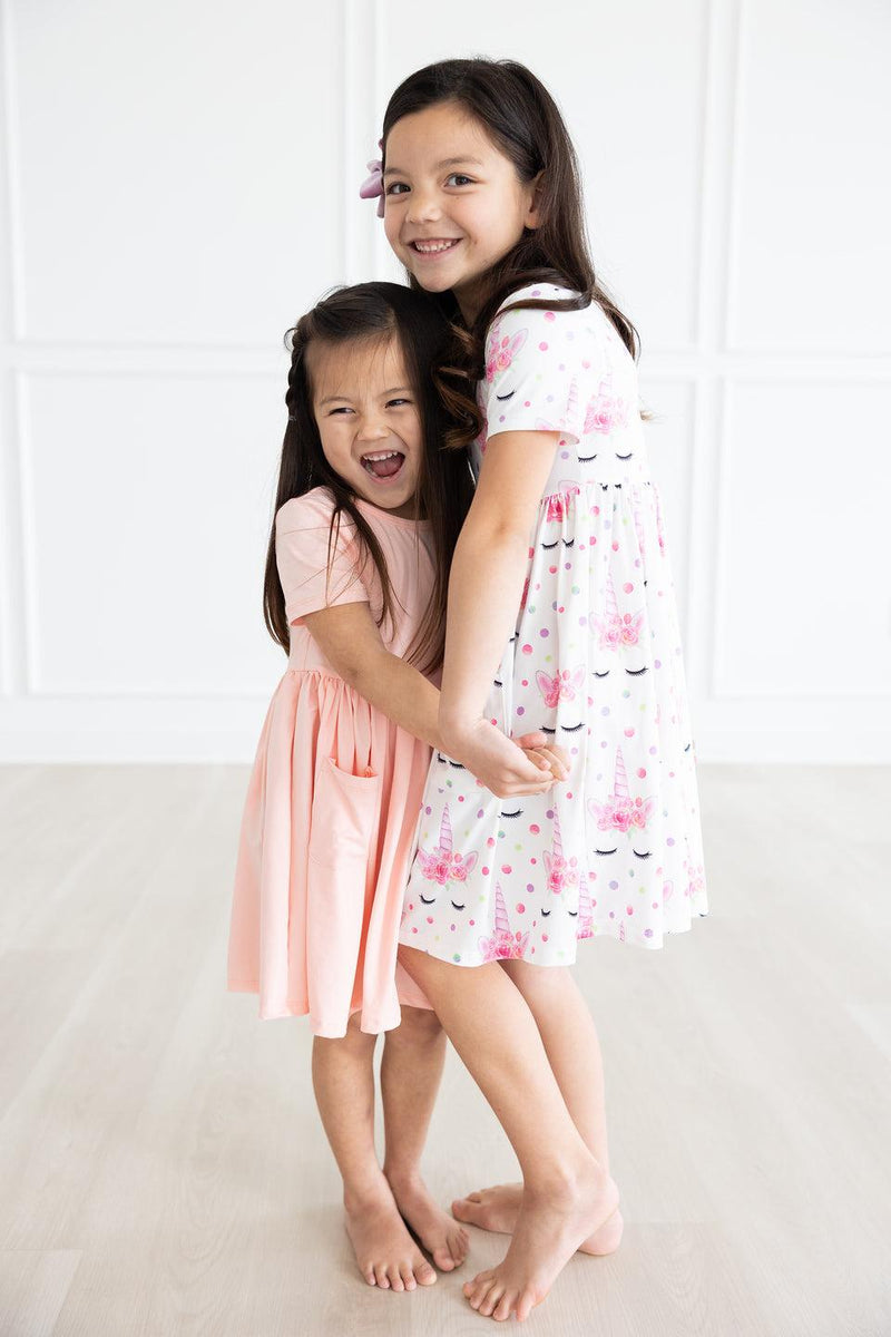 Two happy girls embracing, one wearing a Peach S/S Pocket Twirl Dress by Mila & Rose, the perfect outfit for fun and friendship!