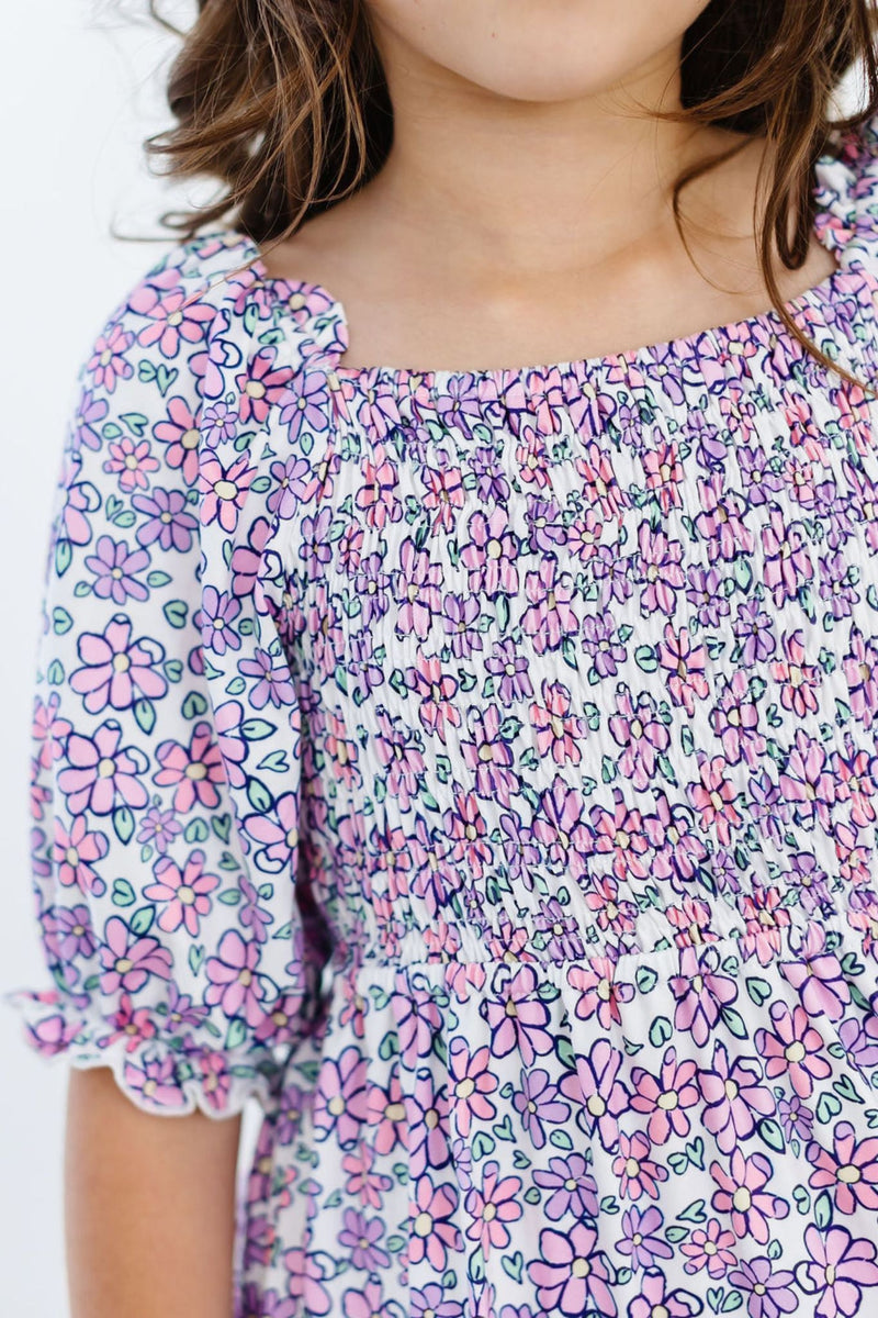 Close-up of a girl's smocked bodice featuring floral patterns on the Lovely Lavender Smocked Ruffle Dress, blending style and comfort.