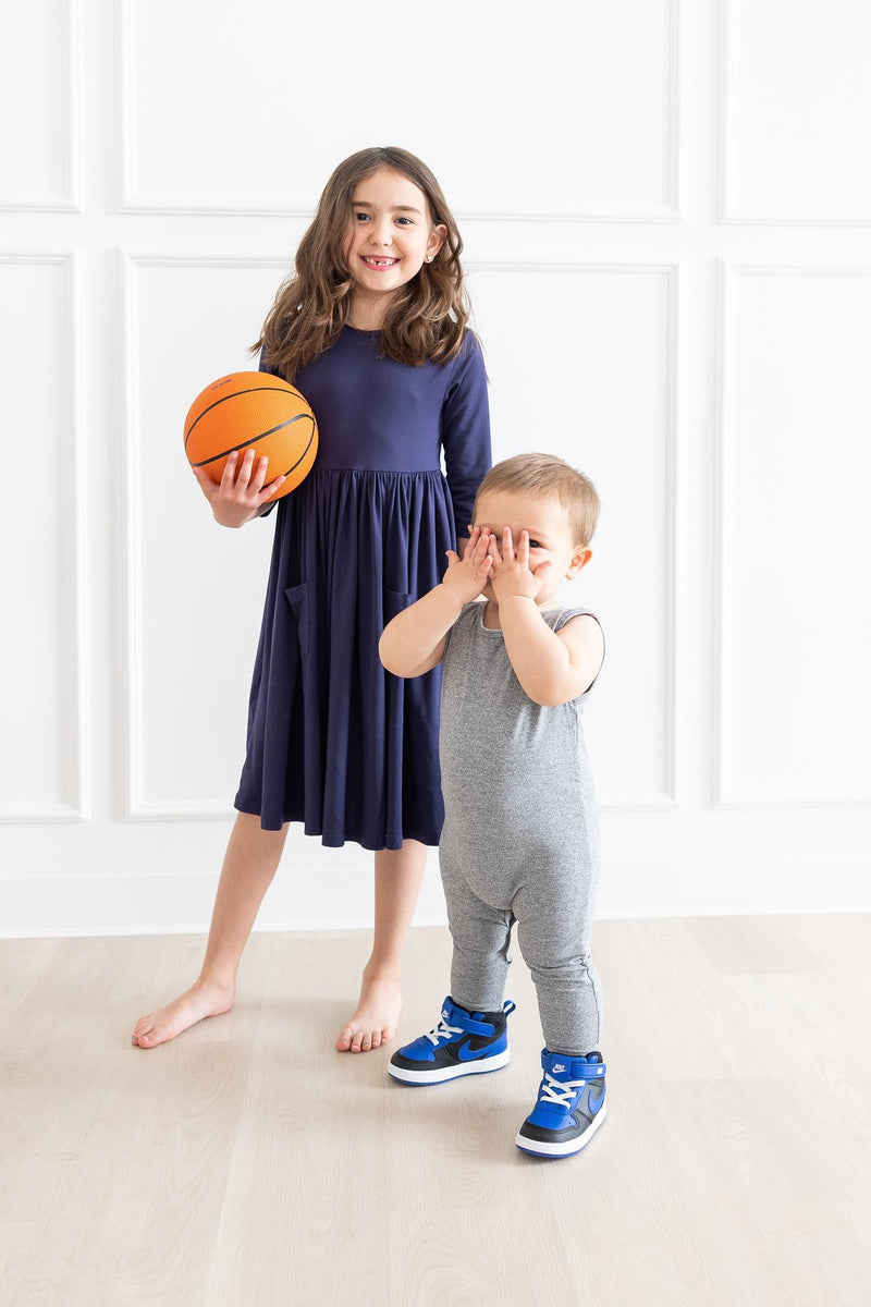 Navy 3/4 Sleeve Pocket Twirl Dress by Mila & Rose®, modeled by a young girl holding a basketball, alongside a toddler in a gray outfit, highlighting playful fashion for kids.