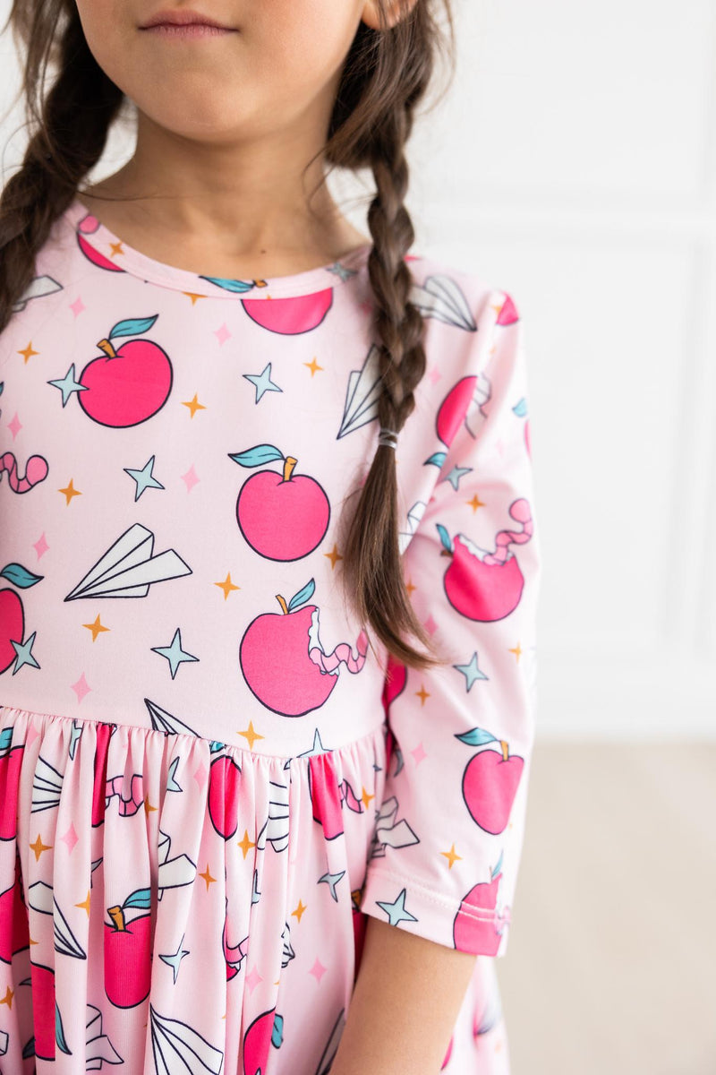 Close-up of a girl wearing the Star Student 3/4 Sleeve Pocket Twirl Dress, showcasing a playful apple and star pattern, ideal for active lifestyles.