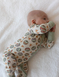 Baby holding sage green convertible cuff of cream zip-up onesie while lying on stomach