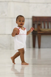 Baby boy wearing white cotton pique romper with red trim and hand-embroidered Christmas holly and berries on pleated yoke.