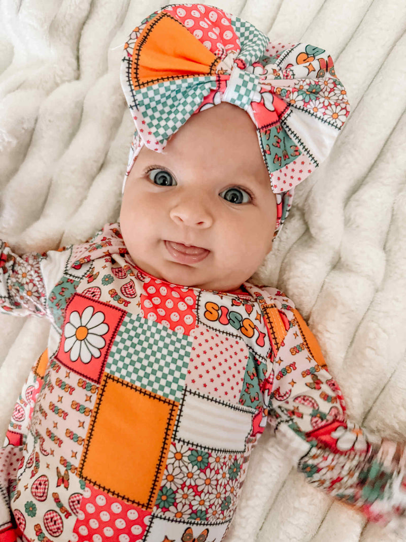 Happy baby enjoying their Anti-Kick 'Sissy' Swaddle Gown & Headband 2 PC Set, with a big bow and colorful patterns. A delightful baby swaddle gown for making memories.